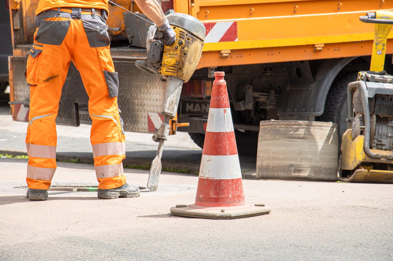 services-02 Construction worker using jackhammer beside traffic cone on urban street